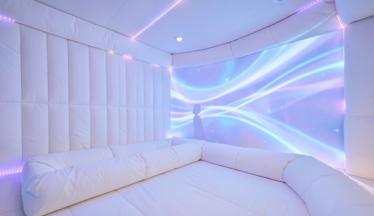Une salle sensorielle capitonnée baignée de lumières douces, avec de grands motifs lumineux bleus et violets projetés sur le mur